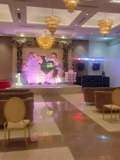 A wide shot showing the scale of a butterfly-themed birthday party in a banquet hall. The decorated stage serves as the main focal point for the event.
