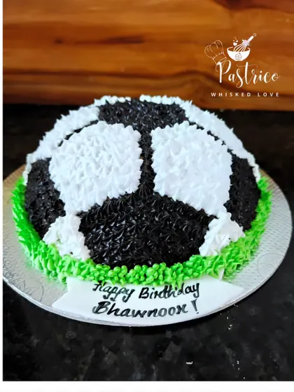 Another view of the football-shaped cake, showing the detailed piping that creates the texture of grass and the ball.