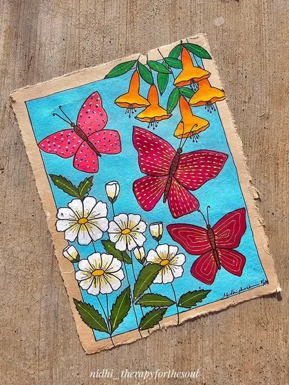 The butterfly painting laid on a wooden surface, showing the texture of the handmade paper and the vibrant colors.
