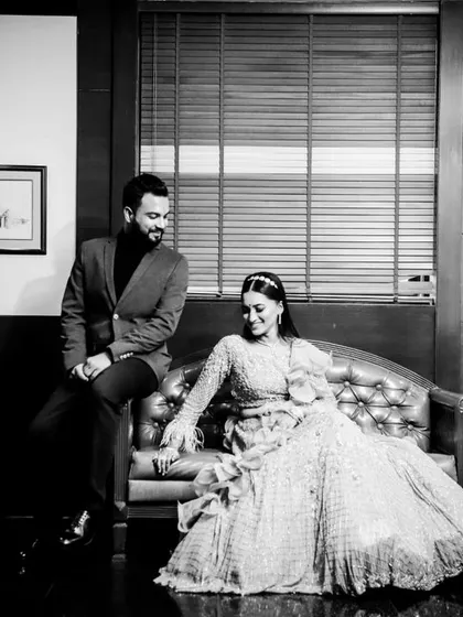 A stylish, posed black and white shot from an engagement. The couple is seated on a vintage leather sofa, creating a classic and sophisticated portrait.