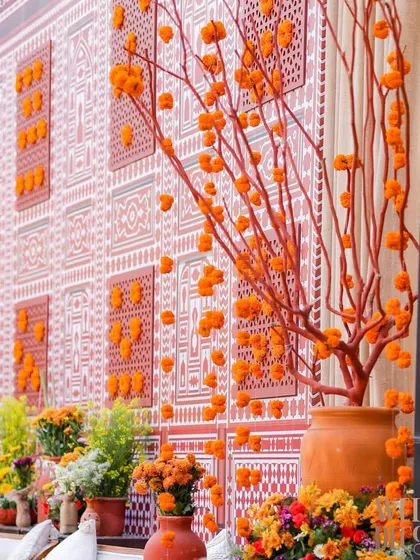 A stunning backdrop wall featuring a custom-printed design inspired by heritage architecture. The wall is accented with 3D panels and marigold clusters, with a beautiful manzanita tree centerpiece.