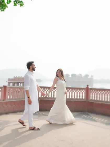 A beautiful pre-wedding photograph taken at Jal Mahal in Jaipur. The couple, dressed in elegant white attire, walks hand-in-hand, creating a timeless and romantic destination wedding memory.