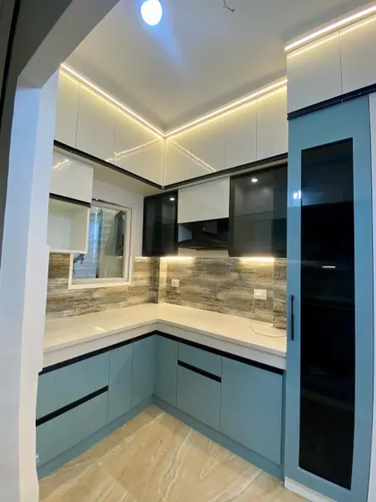 A corner view of a stylish kitchen with light blue and white cabinets, black profile handles, and a tall pantry unit.