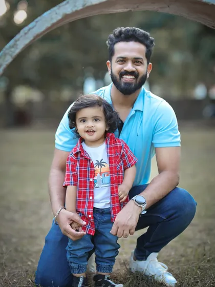 A classic father and son portrait taken outdoors. Both are smiling at the camera, capturing a happy memory in a natural park environment.