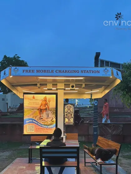 A serene dusk view of our installation at Saryu Ghat. A person rests on the bench, demonstrating the dual function of our huts as both a public utility and an effective out-of-home advertising location.