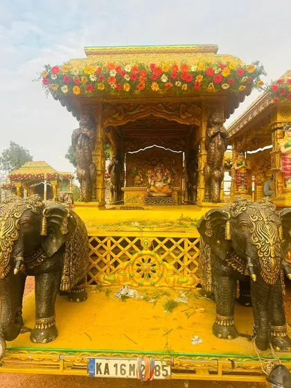 A grand procession chariot with a Ganesha idol, featuring intricately carved elephants and a floral-decorated canopy.