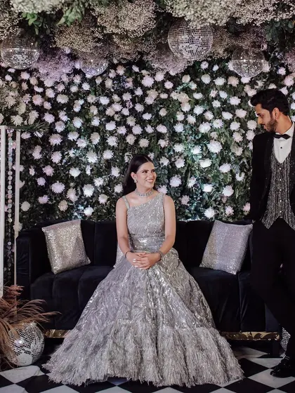 A classic, posed portrait of the couple at their engagement, seated on a stylish sofa against a beautiful floral and disco ball backdrop.
