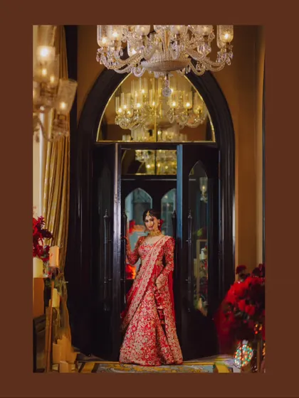 A full-length portrait of the bride in her stunning red lehenga, framed by an ornate doorway.