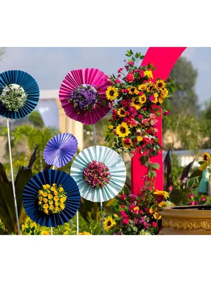 Colorful paper fans with floral centers, a whimsical and creative decor detail for a vibrant Haldi ceremony.
