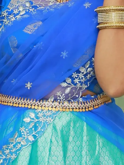 This image focuses on the details of the blue dupatta with silver floral embroidery and the traditional gold waist belt.