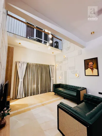 This double-height living room features a stunning green Chesterfield sofa, custom-made with deep button tufting and cane accents. The space is illuminated by modern pendant lighting and a unique, patterned feature wall.