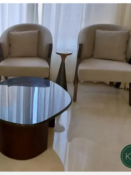A close-up of a seating area featuring two of our custom armchairs. The chairs' gentle curves and neutral fabric create a soft and inviting atmosphere, complemented by a dark wood coffee table.