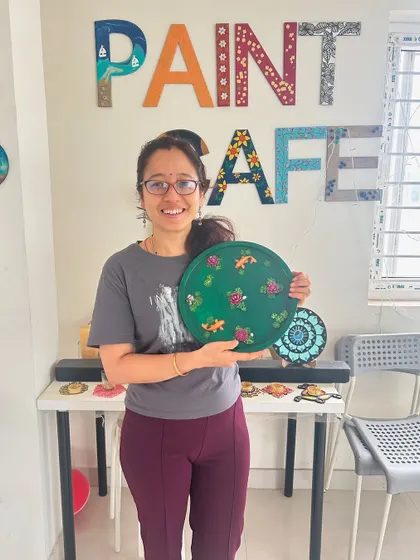 A participant holds up her finished circular painting featuring a floral and fish design.