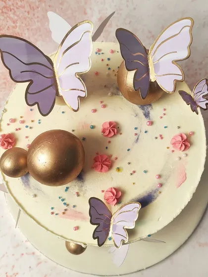 We paint with pastels on this abstract butterfly cake. A watercolor-like blend of pink, purple, and blue buttercream creates a dreamy canvas for delicate purple and gold butterflies and shimmering gold spheres, resulting in a piece of edible art.