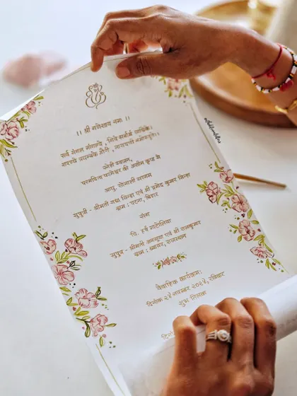 Holding the finished Devanagari invitation. The combination of hand-painted florals and handwritten script on high-quality paper creates a piece that is both beautiful to see and to touch.