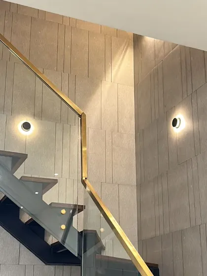 Modern, circular wall sconces are installed on a textured stone wall along a staircase, providing both safety and style.
