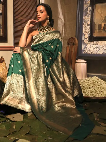 A full-length seated portrait showcasing the magnificent drape of the green and gold Banarasi saree from Soho Begum.
