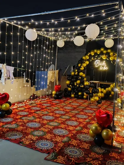 Another perspective of the 'Bride to be' fairy light tent. The black, gold, and red balloon decor adds a touch of glamour to the rustic and romantic lighting setup.