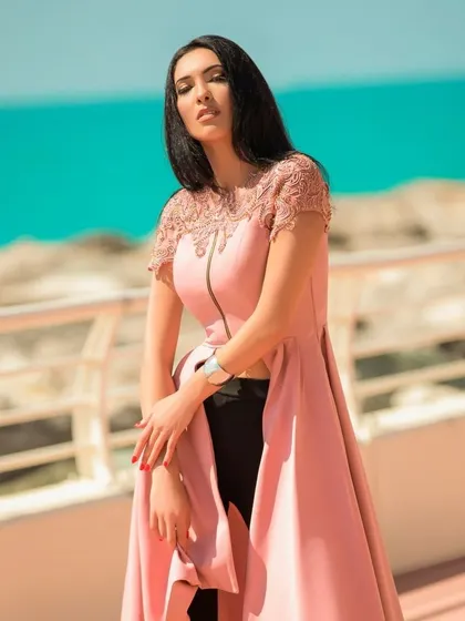 A fashion portrait taken by the sea in Dubai. The bright sunlight and vibrant blue water provide a stunning natural backdrop for the model's pink and black outfit.