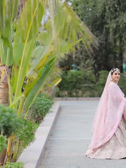 A lovely outdoor portrait of a Sikh couple on their wedding day, holding hands and sharing a smile, perfectly framed by natural greenery.