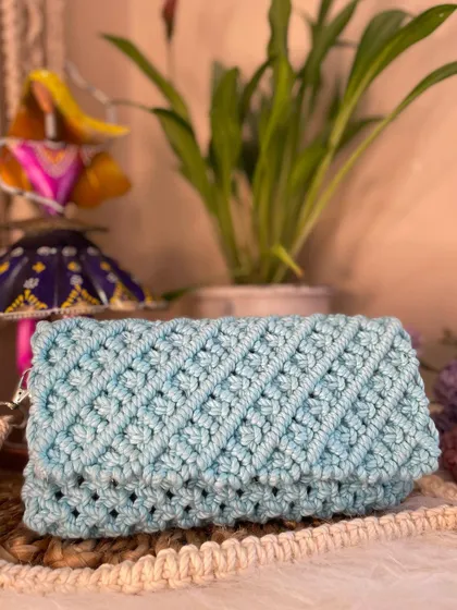 This lovely sky blue macrame clutch features a clean, diagonal knot pattern and a simple flap closure. It can be used as a clutch or worn as a sling for hands-free convenience.