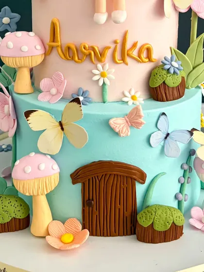 A close-up of the magical details on Aarvika's first birthday cake, showing the tiny fairy door, handcrafted mushrooms, and delicate wafer-paper butterflies.