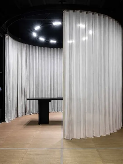 A view of the retail gallery showing the interplay between the dark, austere material palette and the soft, translucent curtains. The design fosters an ambiance of quiet luxury and calm, encouraging slow, mindful discovery.