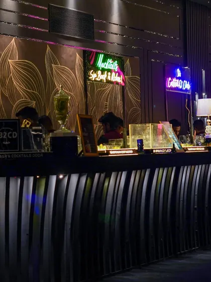 The stylish bar area, featuring a modern, fluted bar front and vibrant neon signs. This setup combines sleek design with a fun, club-like atmosphere.