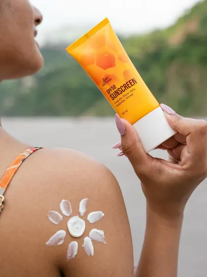 A lifestyle shot showing the application of sunscreen. The sun-shaped cream on the model's shoulder is a playful and creative way to demonstrate the product's use.