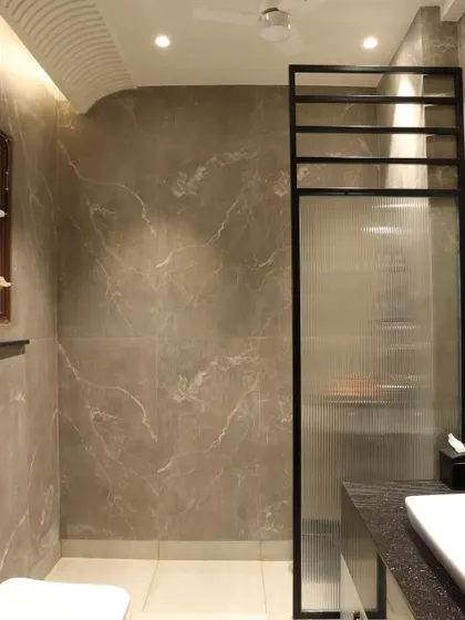 A fluted glass partition with a black metal frame separates the shower area, adding a touch of industrial chic to the elegant space.
