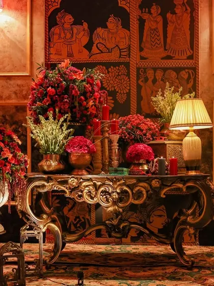 An ornate console table adorned with large floral arrangements and traditional Indian art panels on the wall. This vignette combines classic furniture with heritage motifs to create a timeless and elegant corner.