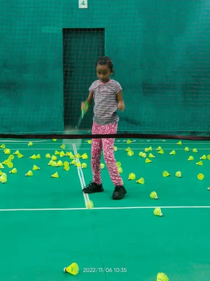 A young girl stands ready on the court, surrounded by shuttlecocks after an intense multi-feed drill. This is a common sight during our focused training sessions.