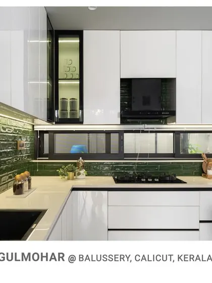 Another view of the Gulmohar kitchen, highlighting the glossy white cabinetry, under-cabinet lighting, and the refreshing green backsplash that adds a pop of color.