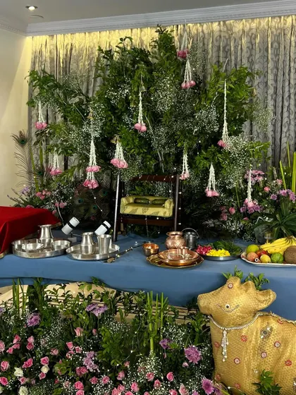 A complete view of our elegant Janmashtami setup. The altar table is draped in blue fabric, with a backdrop of lush green foliage and hanging floral tassels, creating a serene and beautiful space for worship.