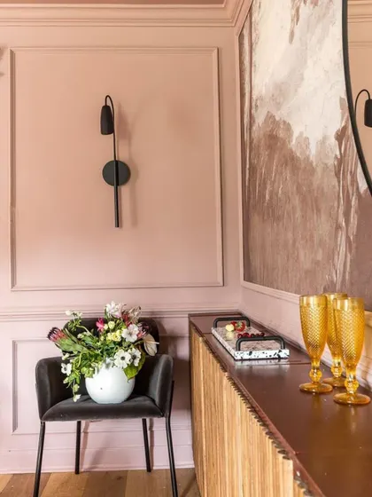 An example of an earthy pink palette in action. The wainscoted walls, paired with a modern black sconce and a wooden console, create a look that is both classic and contemporary.