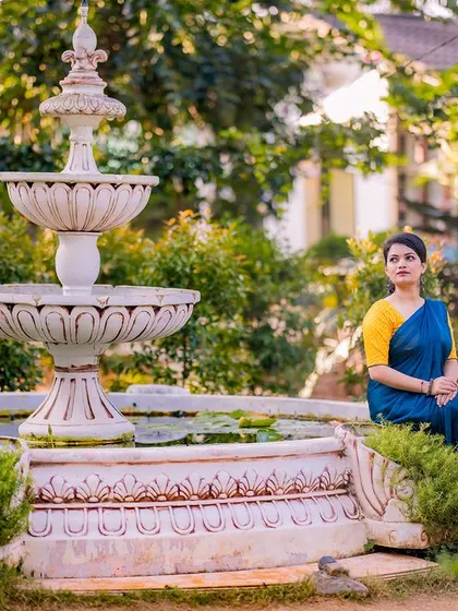 A classic portrait by a beautiful white fountain. The couple's vibrant yellow and blue traditional outfits create a striking color combination in this serene garden setting.