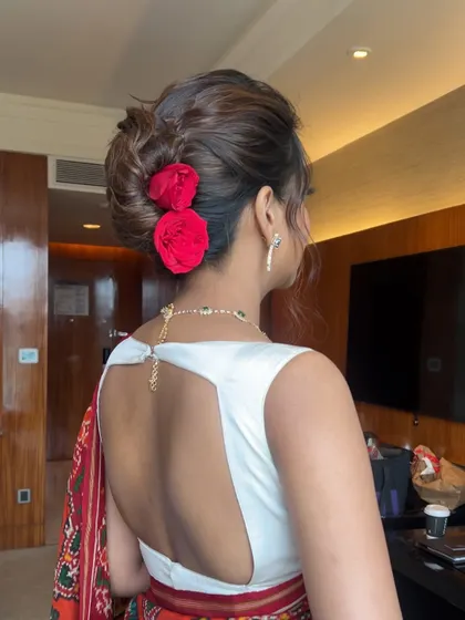 A classic low bun adorned with two bright red roses. This is a bold and romantic statement, perfect for a reception or engagement.