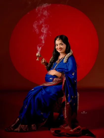 Looking directly at the camera, this portrait captures the confidence and joy of the mother-to-be in her royal blue saree, holding a traditional dhuni.