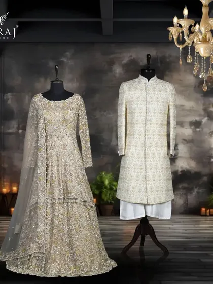 A coordinated vision of elegance. The groom's off-white silk sherwani with delicate zardozi detailing provides a classic foundation, while the bride's beige net Indo-Western gown shines with opulent stone and mirror work.
