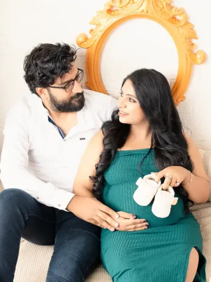 A cozy and sweet moment. The couple sits together, holding a pair of tiny baby shoes, their expressions full of warmth and anticipation.