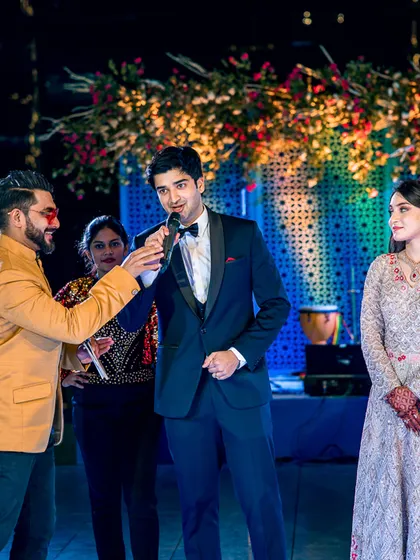 Capturing the interactive and fun moments of a Sangeet night, as the event host engages with the groom on stage.