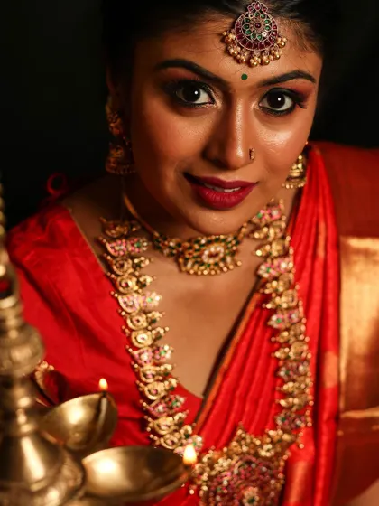 This Kemp jewelry set, with its vibrant red and green stones, is perfect for a classic bridal look. The set includes a choker, a longer haram with a large pendant, and a matching maang tikka, shown here by the warm light of a traditional lamp.