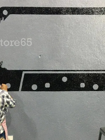 An artist from our team carefully painting the outline of a large cassette tape graphic for a gym mural. We use stencils and freehand techniques to get the shapes just right.