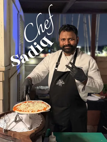 This is Chef Sadiq, one of our pizza specialists. Here he is at an outdoor event, proudly presenting a freshly made cheese pizza, ready for the oven.