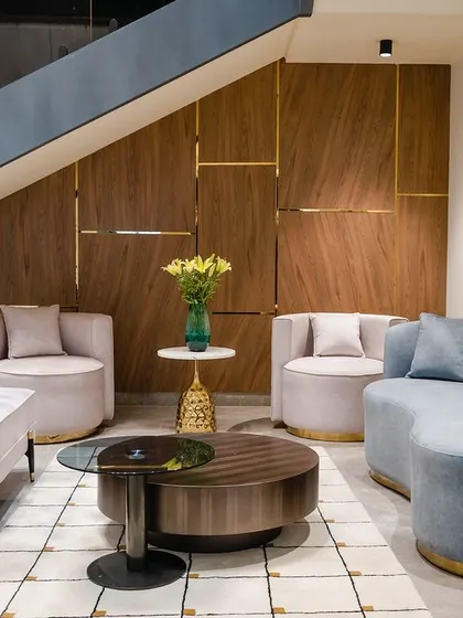 A 3D render of a stunning seating area under a staircase. The mix of blush pink and dusty blue sofas against a wood-paneled wall with gold accents is pure elegance.
