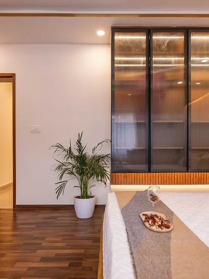 This elegant bedroom uses a warm brown and beige color palette. The design features a large glass-fronted wardrobe that makes the space feel bigger, complemented by rich wooden flooring.