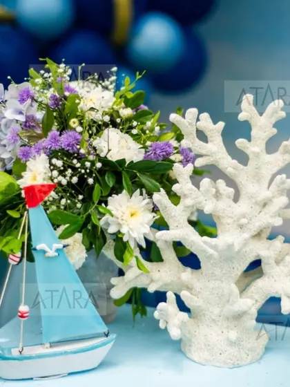 A close-up of a nautical-themed centerpiece. A miniature sailboat and a piece of white coral are placed next to a beautiful floral arrangement, showing the attention to detail.