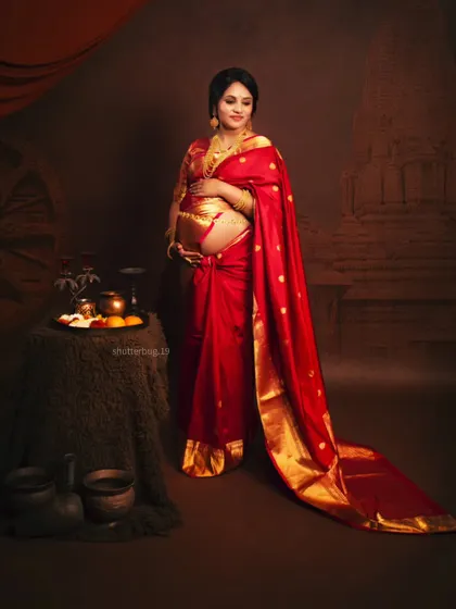 Another angle from our traditional saree shoot, showing the full setup with antique-style props and a temple-themed backdrop. The mom-to-be looks radiant holding her bump.