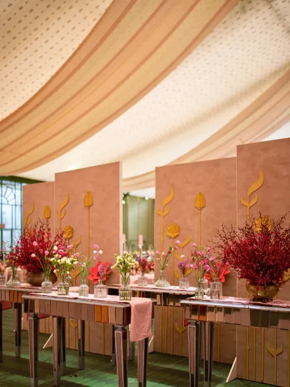 The serene reception dinner setting, with mirrored console tables and minimalist floral arrangements against a textured pink wall.