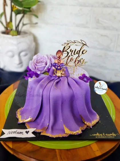 A gorgeous "Bride to Be" cake featuring a fondant doll with a flowing purple gown and gold accents. It's an elegant and personal cake for a bachelorette party or bridal shower.